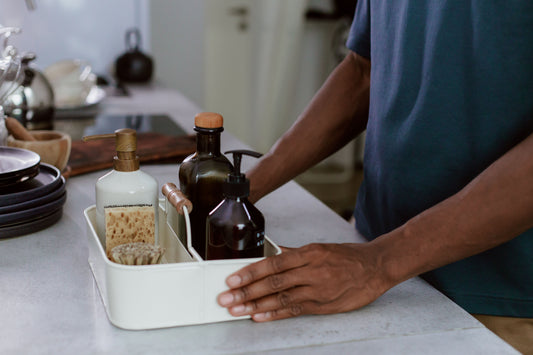 Hands arranging cleaning bottles and a sponge in a caddy in a home kitchen