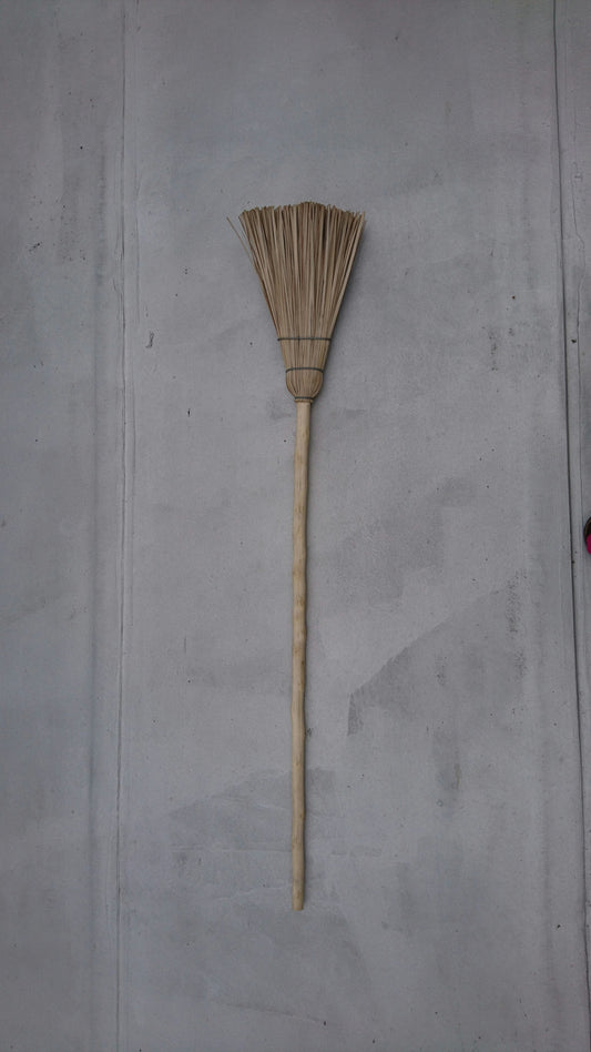A straw broom leaning against a plain wall