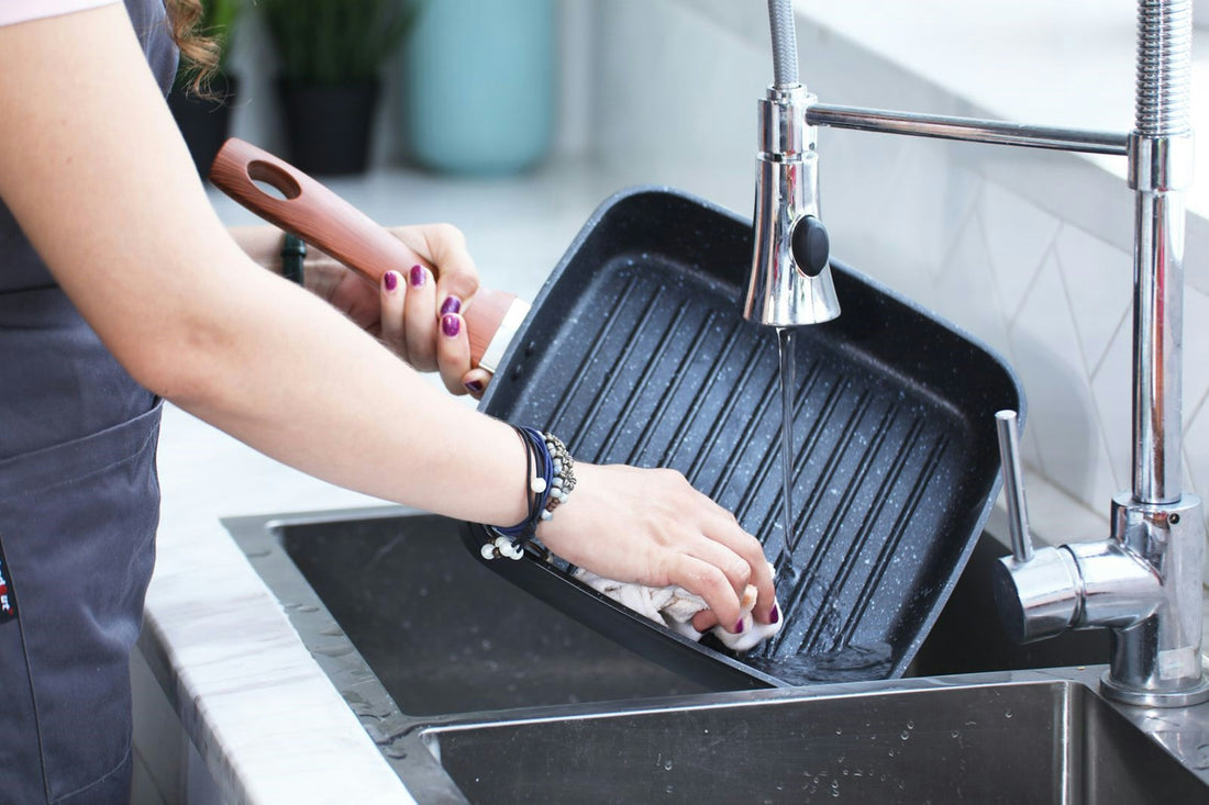 A person washing a pan at a kitchen sink