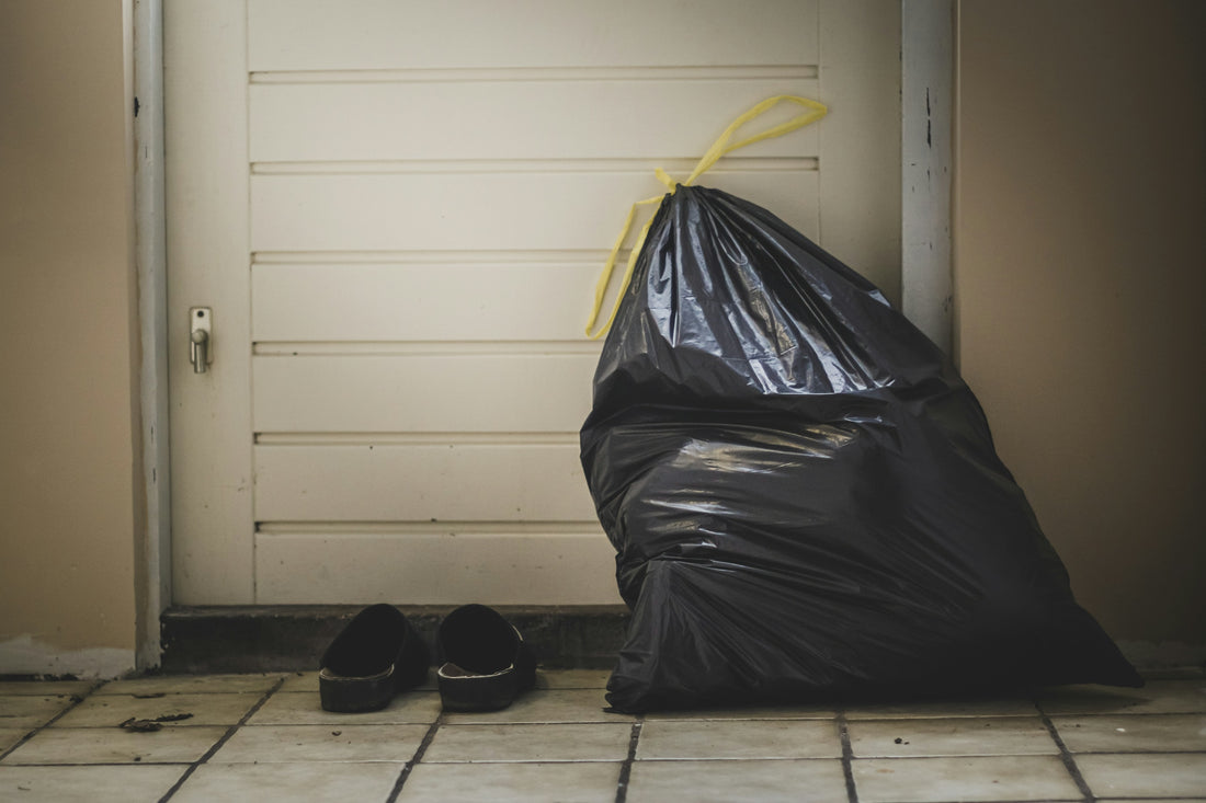 A full black trash bag with a twist tie by a front door