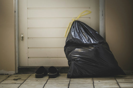 A full black trash bag with a twist tie by a front door