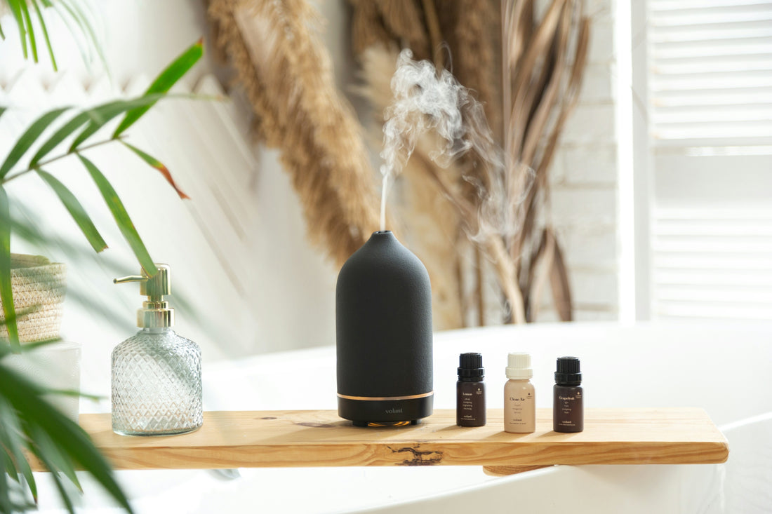 A black essential oil diffuser releasing mist next to bottles on a wooden shelf