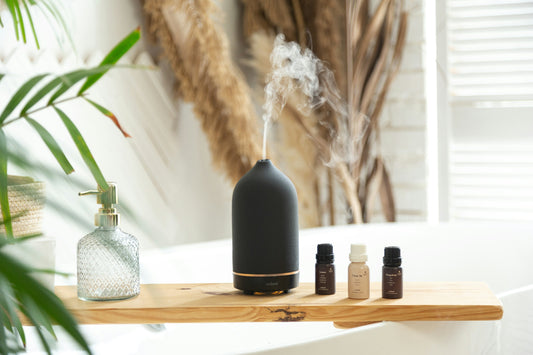 A black essential oil diffuser releasing mist next to bottles on a wooden shelf