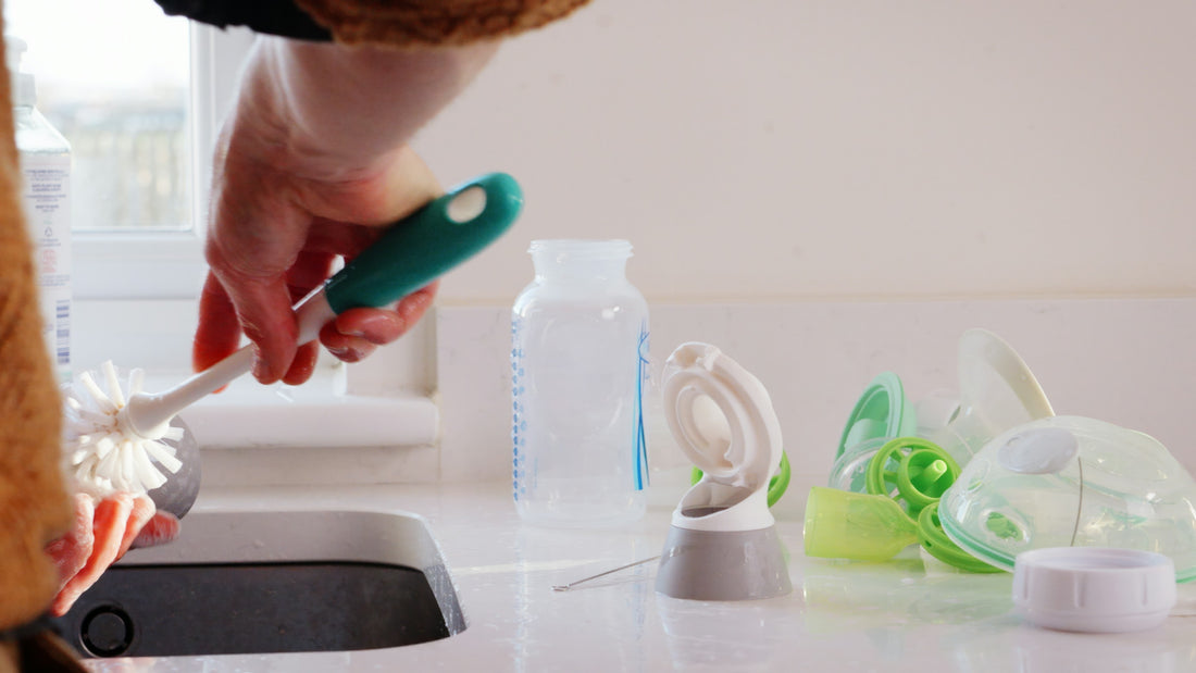 A hand using a bottle brush to clean a bottle at a sink