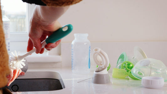 A hand using a bottle brush to clean a bottle at a sink