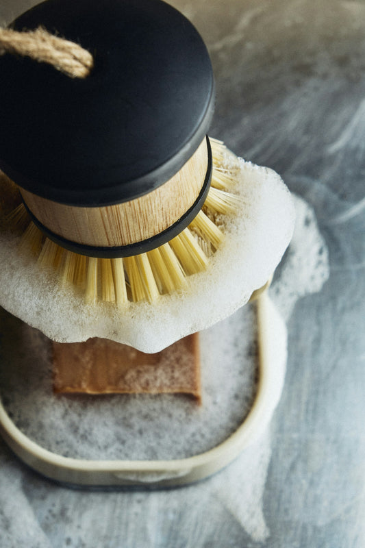 A wooden dish brush resting on a soap bar with suds
